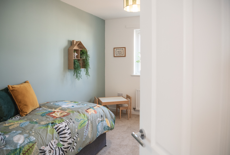 A child's bedroom with a bed, a small table and chairs, and a decorative shelf.