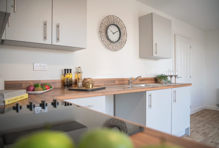 A modern kitchen with light gray cabinets, a wooden countertop, and a stainless steel sink.