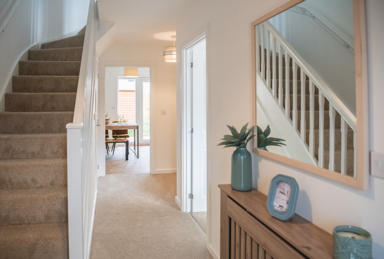 A hallway with a carpeted staircase, a mirror, and a doorway leading to a dining area.