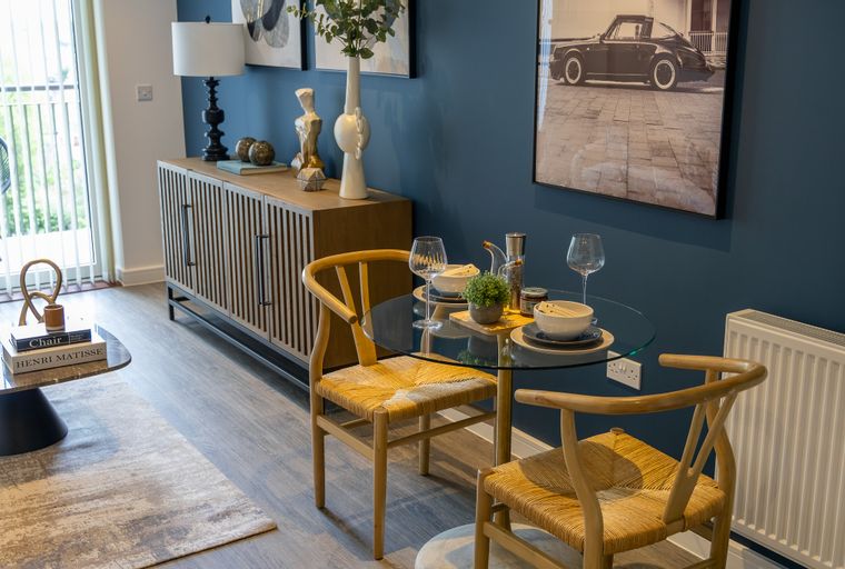 A dining area with a glass-top table, wooden chairs, and a sideboard.
