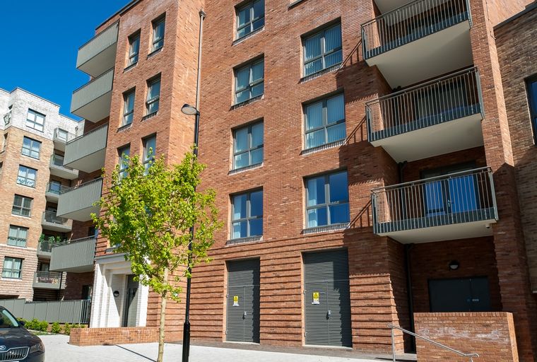 A modern brick apartment building with balconies and garages under a clear blue sky.