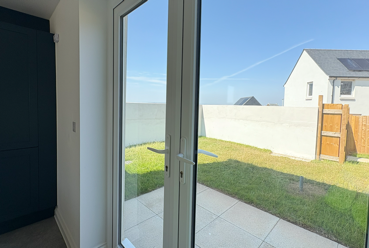 A view through French doors to a backyard with a patio, lawn, and a wooden gate.