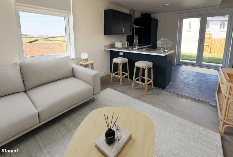 A living room and kitchen area with a sofa, coffee table, kitchen island with stools, and a door leading outside.