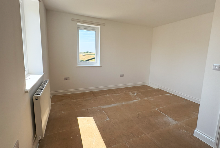 A bedroom with a window, radiator, and unfinished floor.