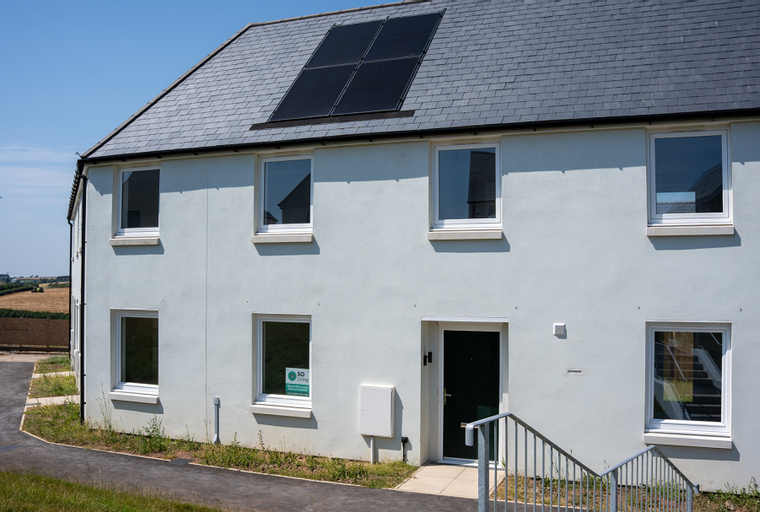 A modern house with solar panels on the roof and several windows.