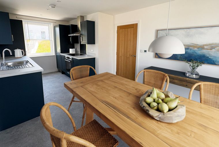 A kitchen and dining area with navy cabinets, a wooden table, and wicker chairs.