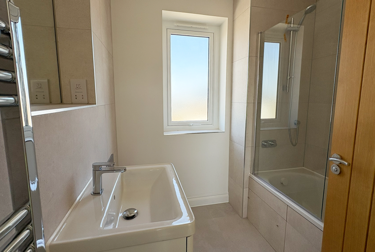 A bathroom with a sink, bathtub, shower, window, and towel rack.
