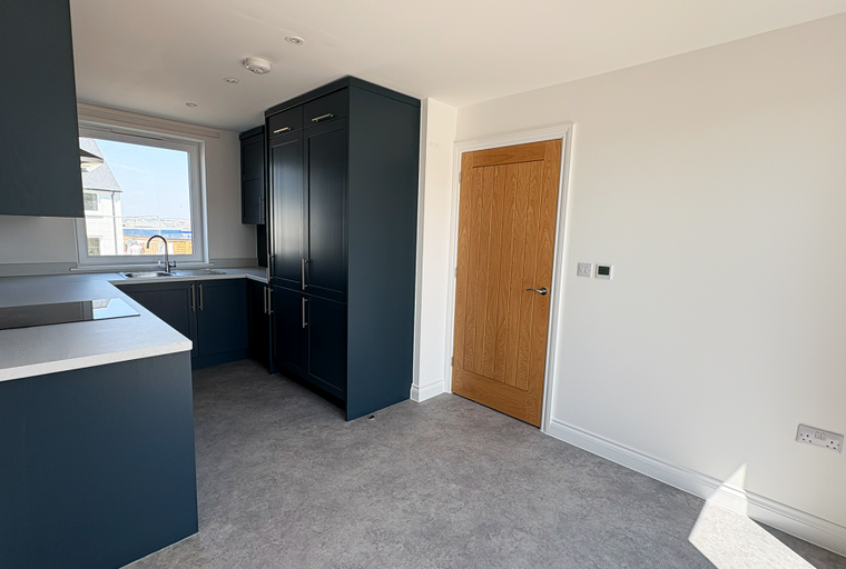 A modern kitchen with dark blue cabinets, a countertop with a hob, a sink, and a wooden door.