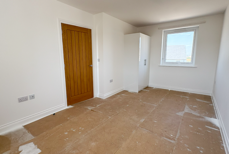 A bedroom with a wooden door, a white wardrobe, and a window.