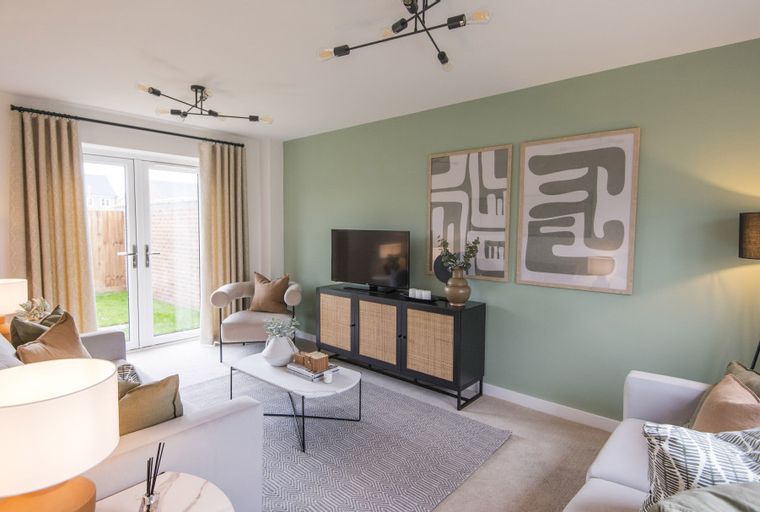 A living room with a television, media console, coffee table, sofas, armchair, and double doors leading to a garden.
