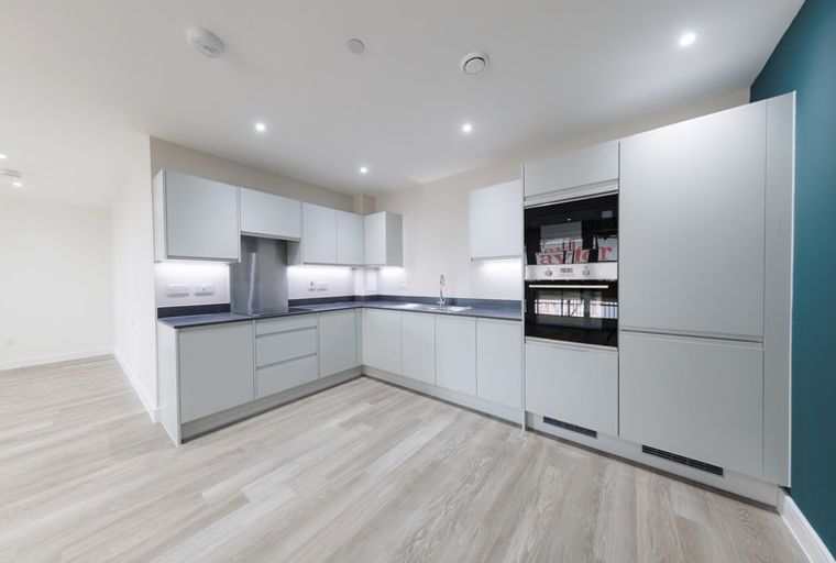 A modern L-shaped kitchen with light grey cabinets, dark countertops, and integrated ovens.