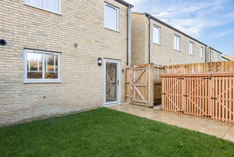 A backyard with a lawn, patio, wooden storage unit, and fence.