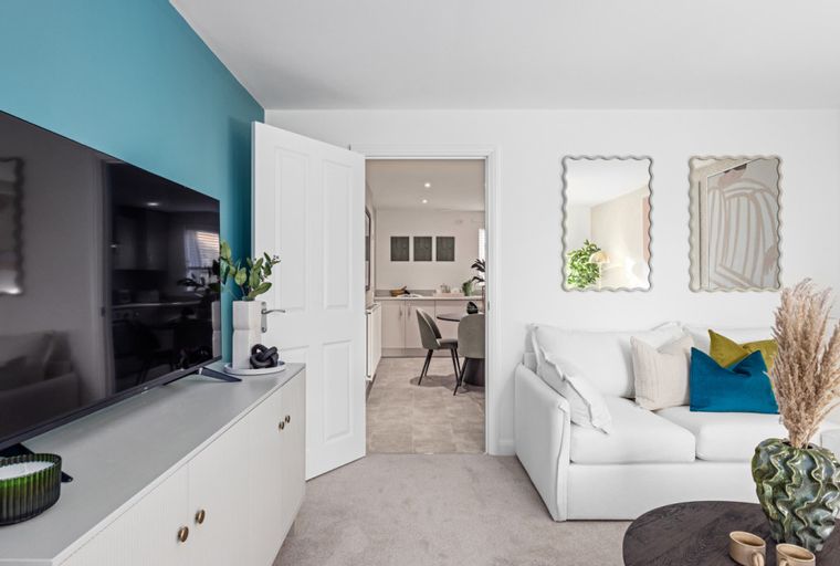 A living room with a TV, sofa, and an open doorway to a kitchen.