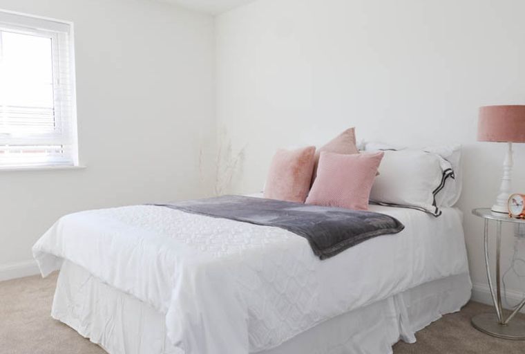 A bedroom with a bed, pillows, a throw blanket, a bedside table, and a lamp.