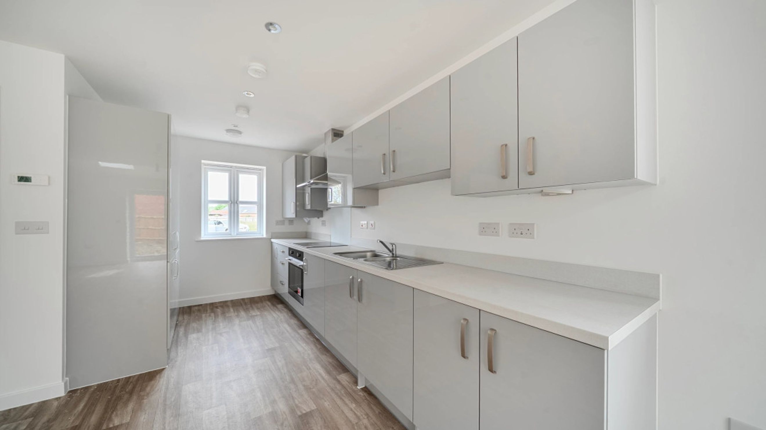 A modern kitchen with light grey cabinets, a countertop, a sink, and a window.