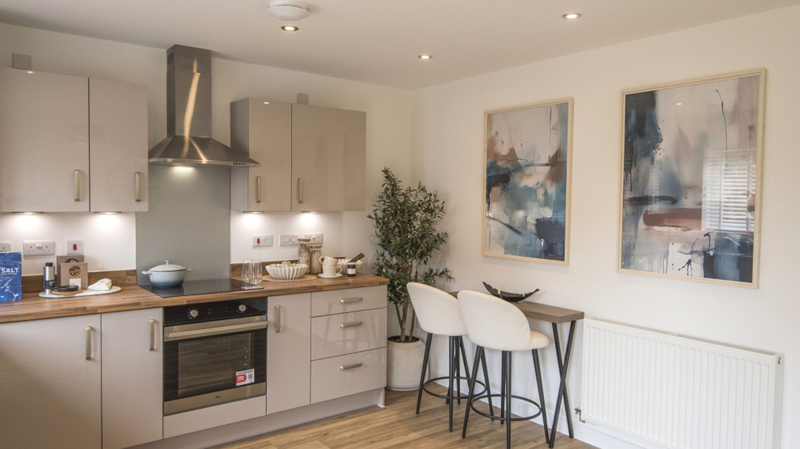 A modern kitchen with light-colored cabinets, a stainless steel range hood, an oven, and a breakfast bar with two stools.