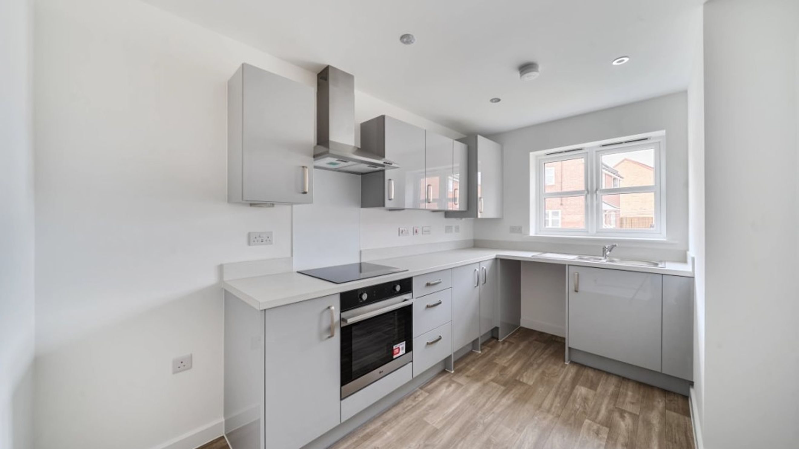 A modern kitchen with grey cabinets, a built-in oven, and a sink under a window.