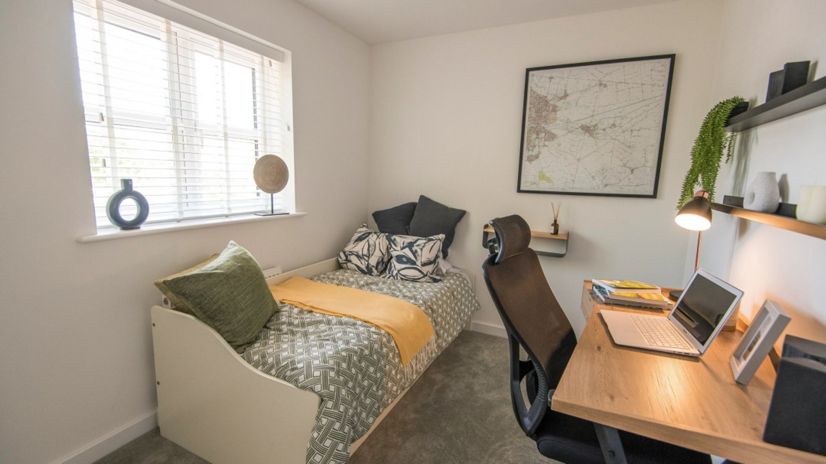 A bedroom with a single bed, a desk with a laptop, and a window.