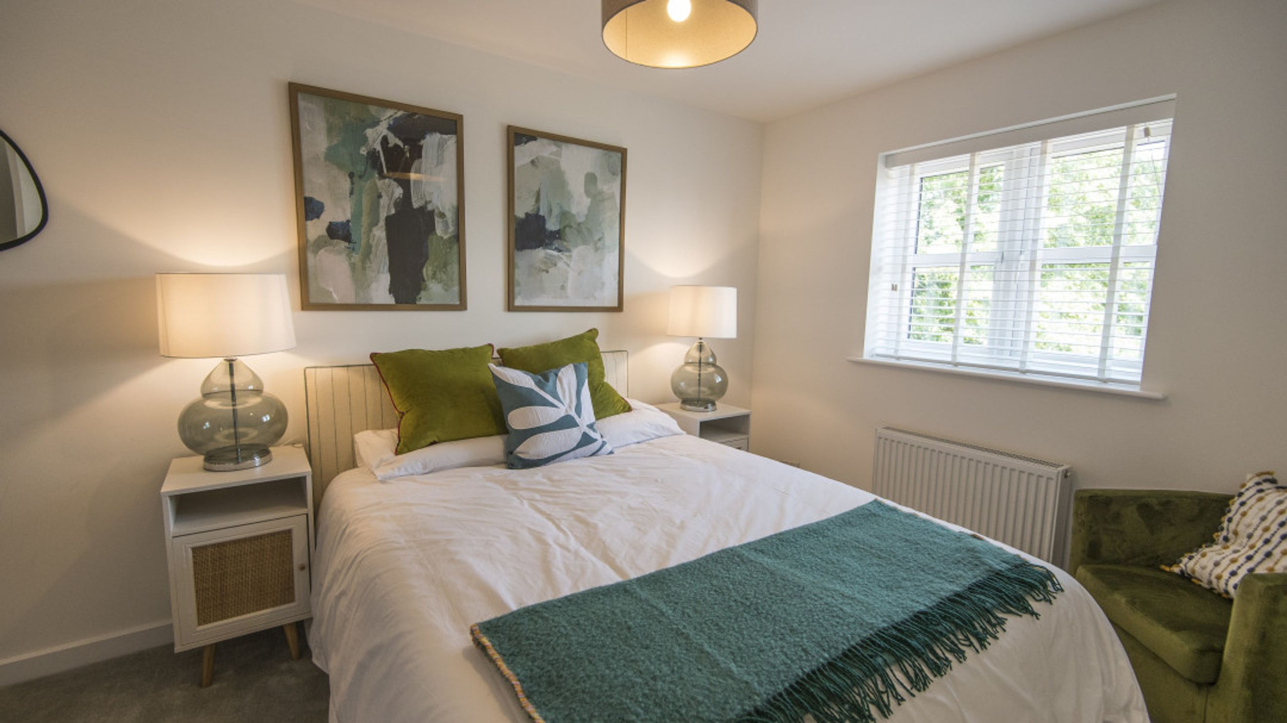 A bedroom with a bed, bedside tables, lamps, artwork, a window, and a chair.