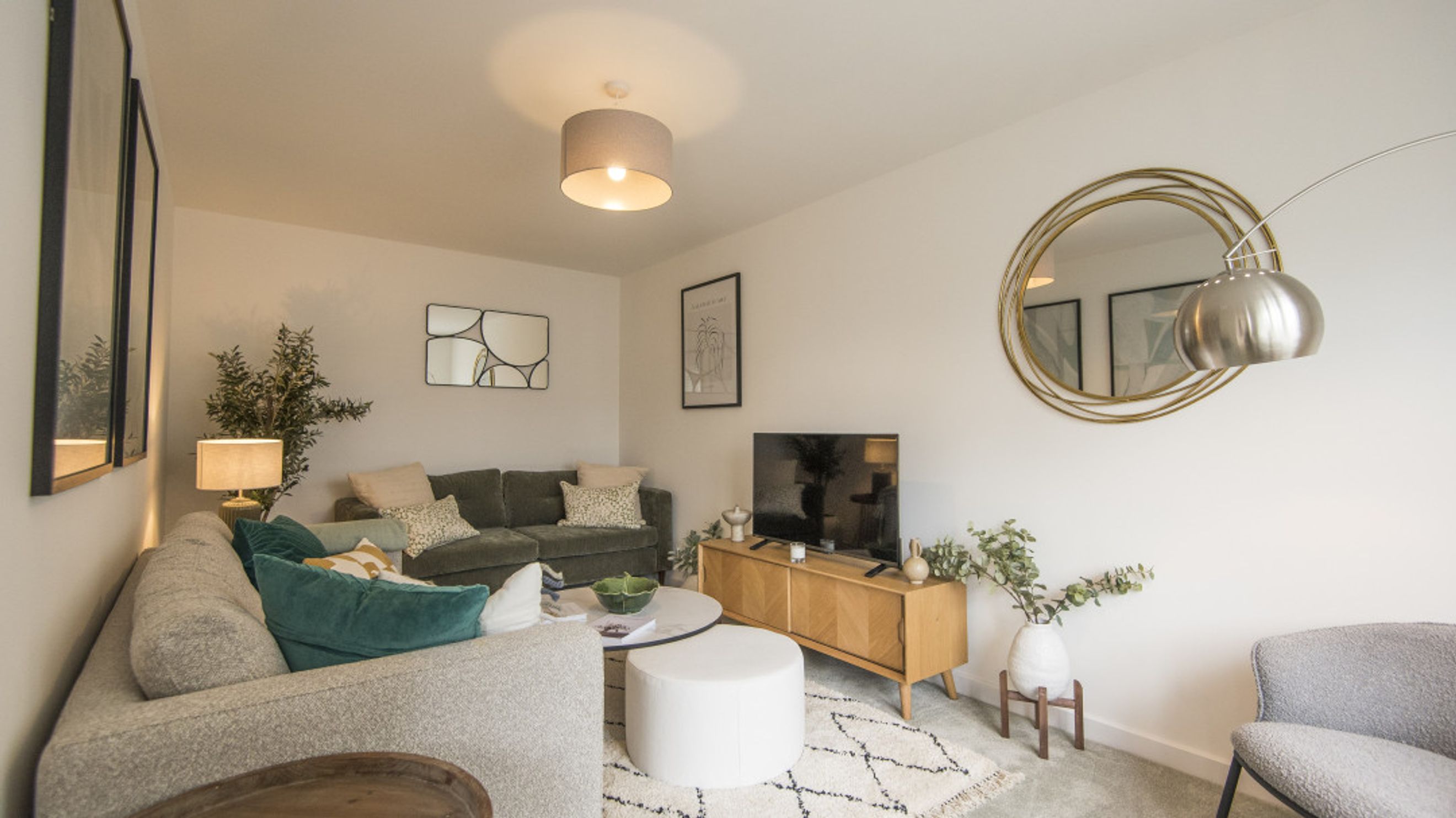 A living room with a sectional sofa, TV, media console, and a circular mirror.