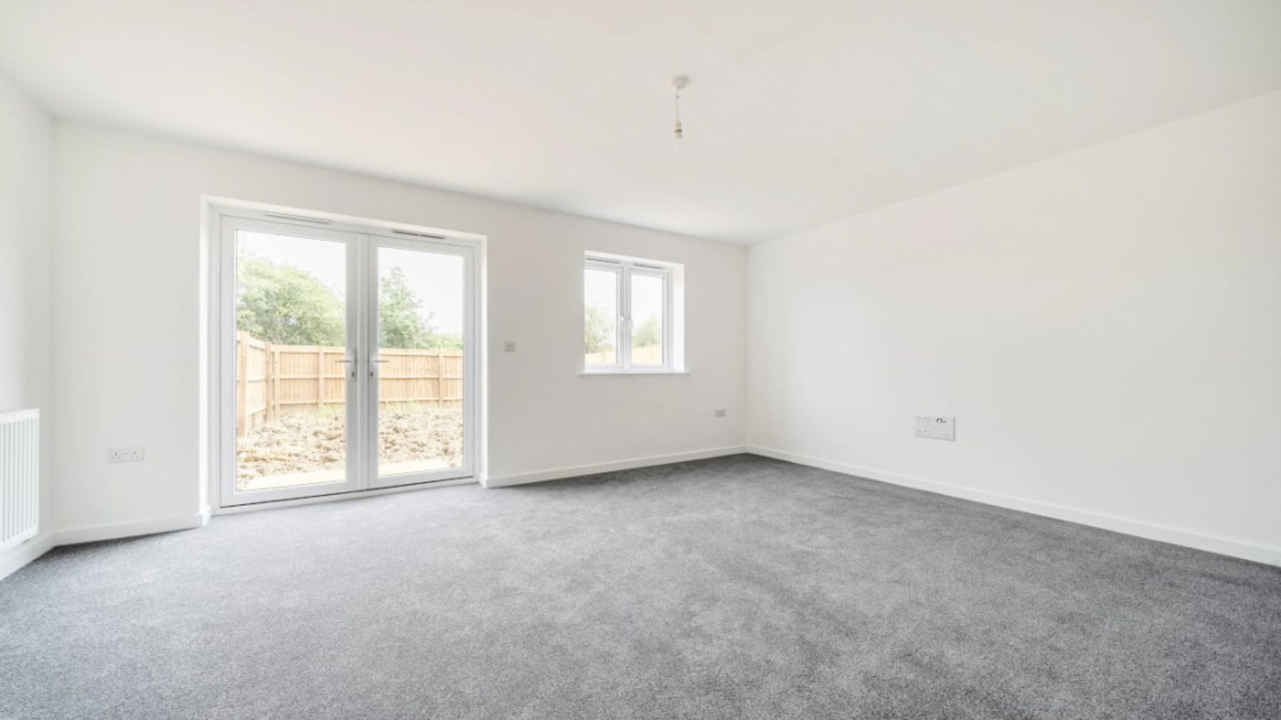 A living room with grey carpet, white walls, and double doors leading outside.