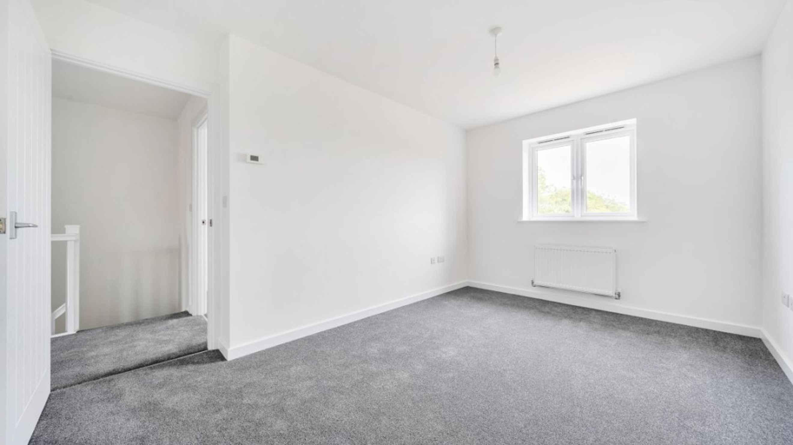 A bedroom with grey carpet, white walls, and a window.