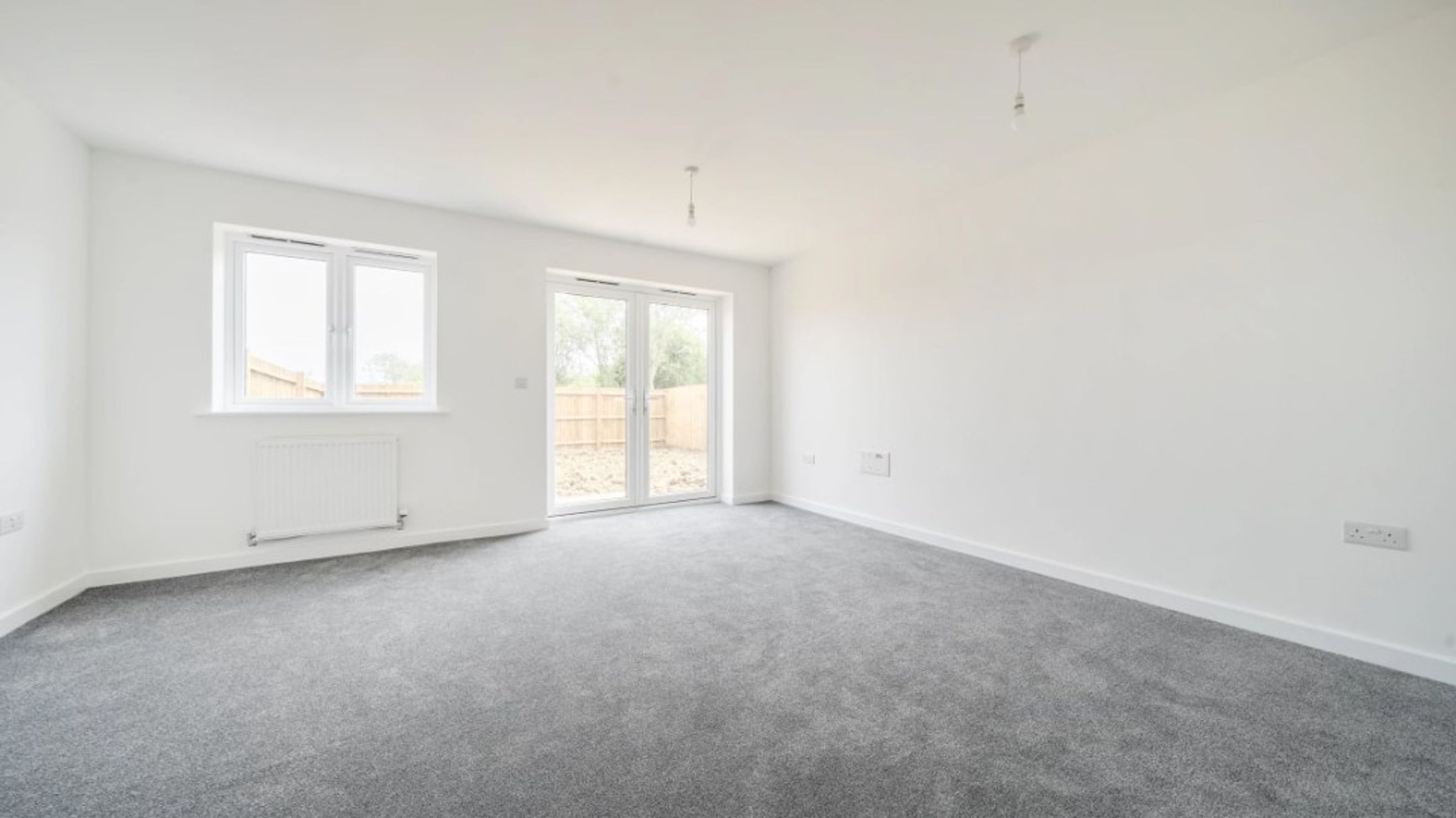 A living room with grey carpet, white walls, a window, and patio doors.