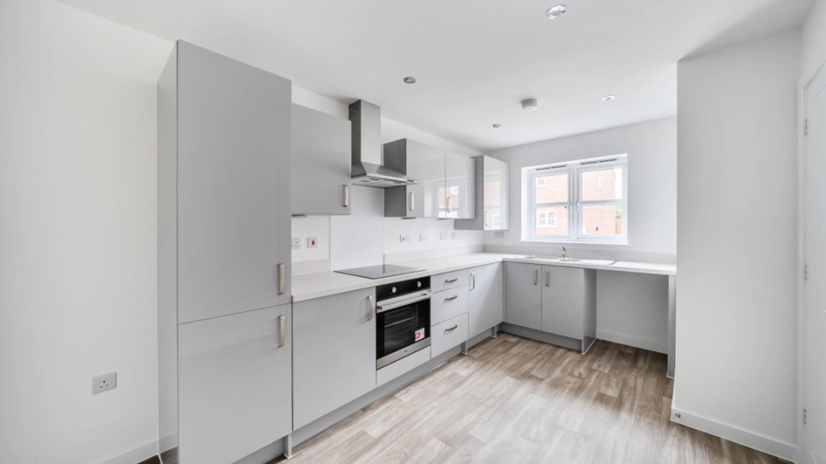 A modern kitchen with grey cabinets, a built-in oven, and a window.