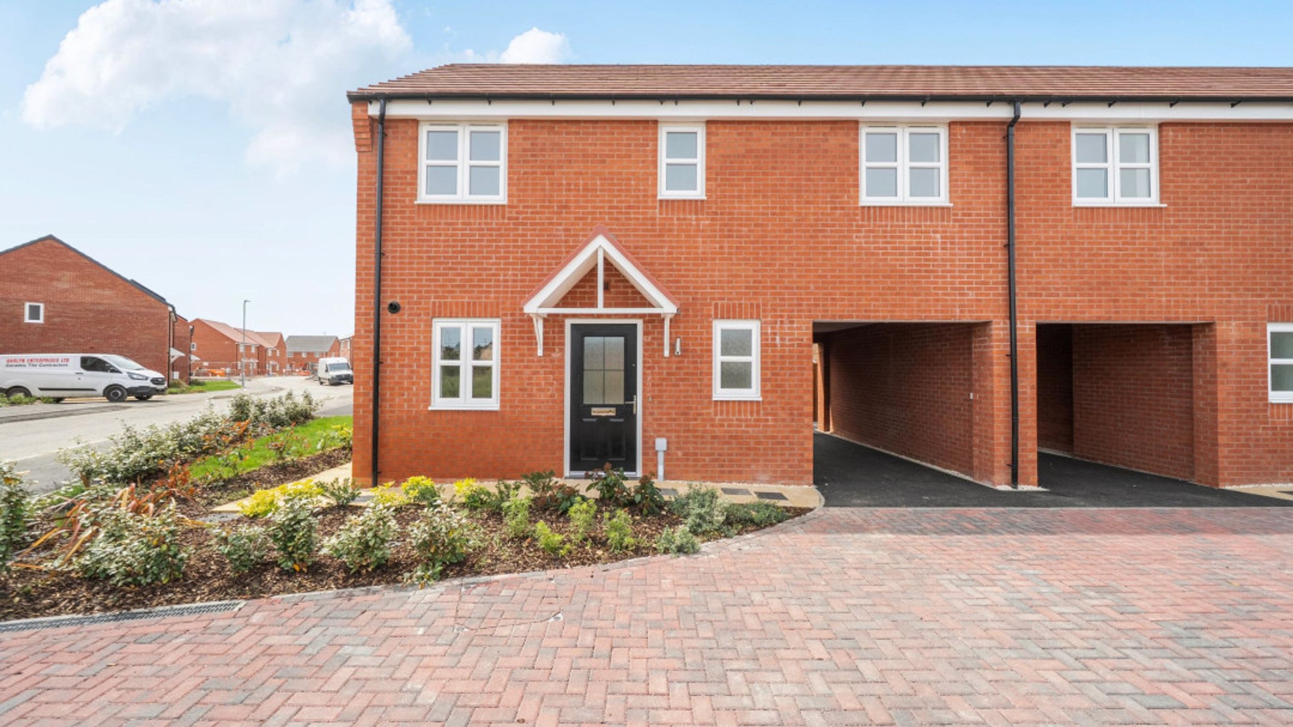 A red brick townhouse with a black front door, white-framed windows, and a car port.