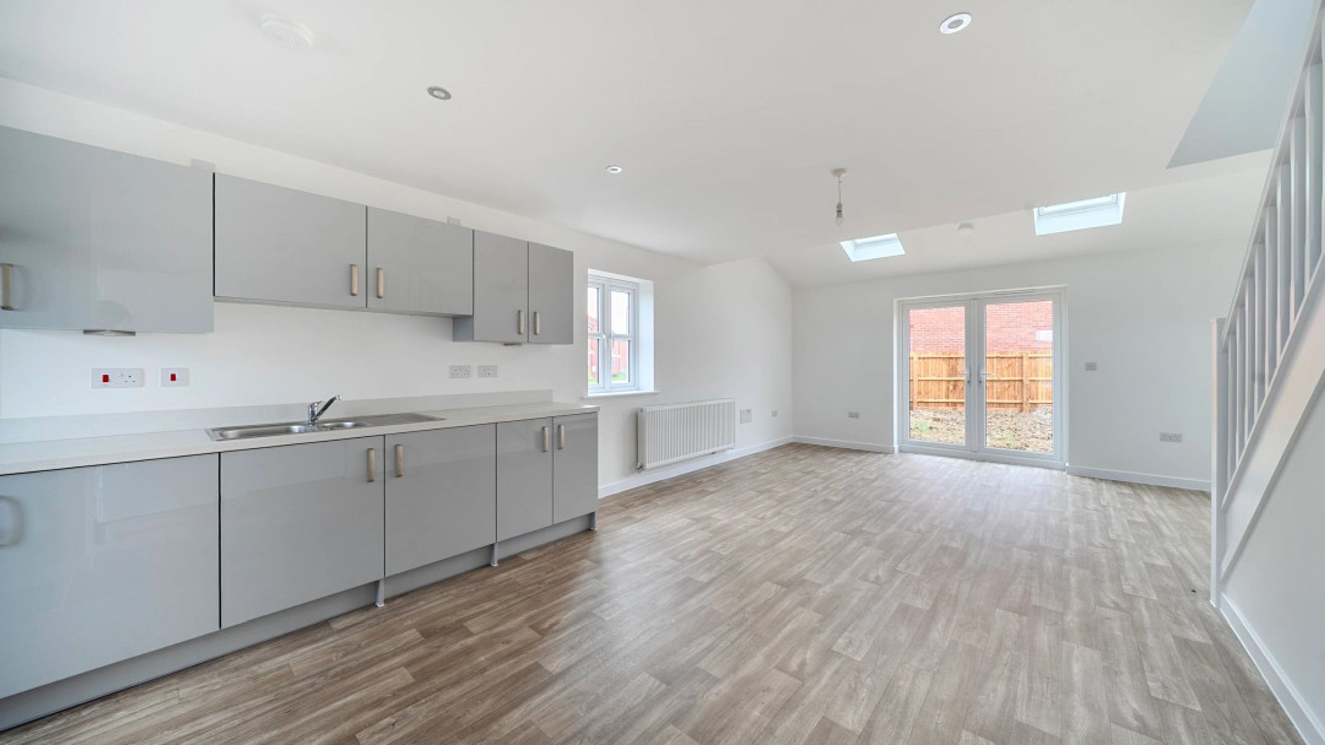 A modern open-plan kitchen and living area with grey cabinets, a sink, and double doors leading to a garden.