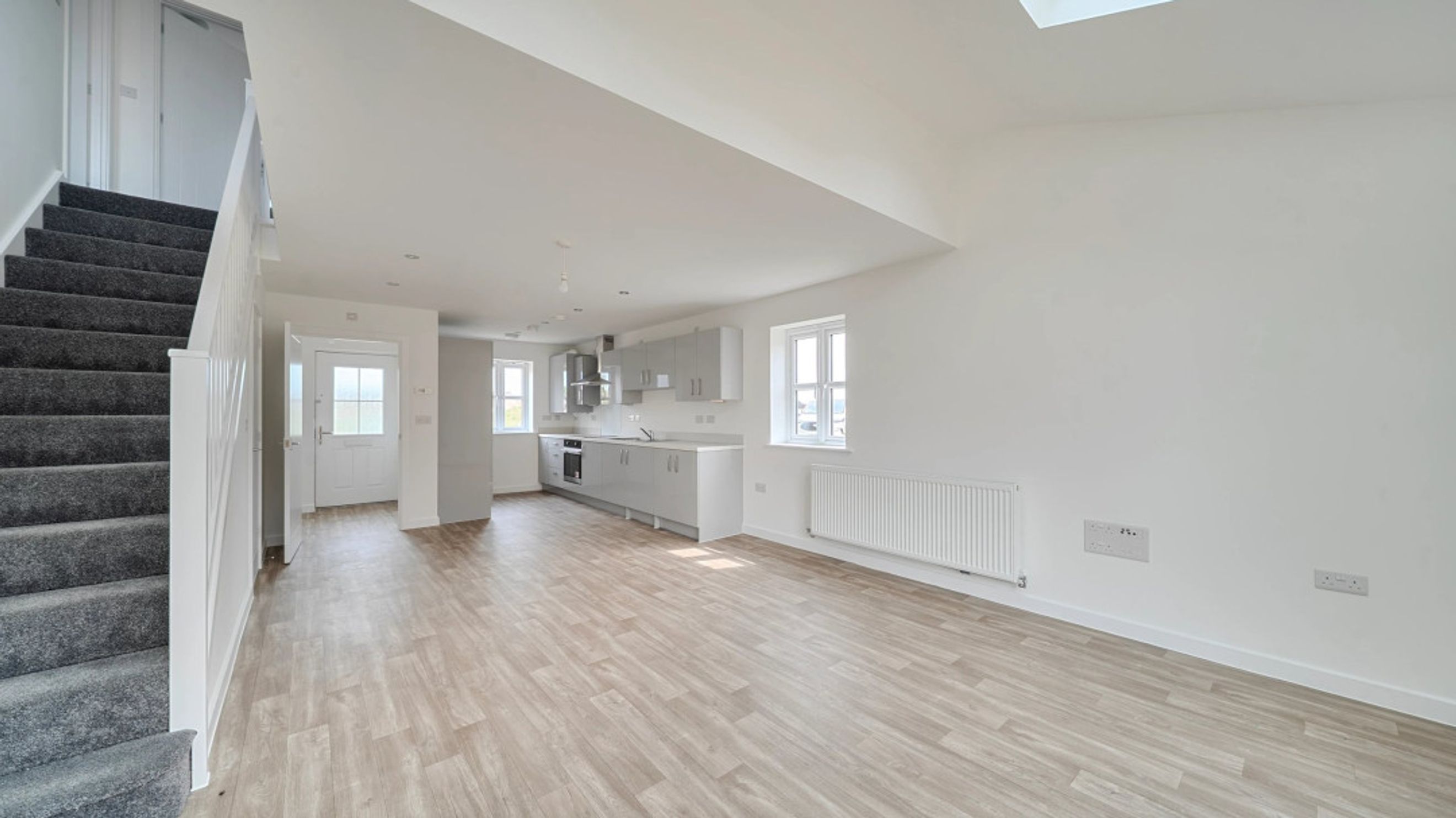 A modern open-plan living area and kitchen with a carpeted staircase and an entrance hall.