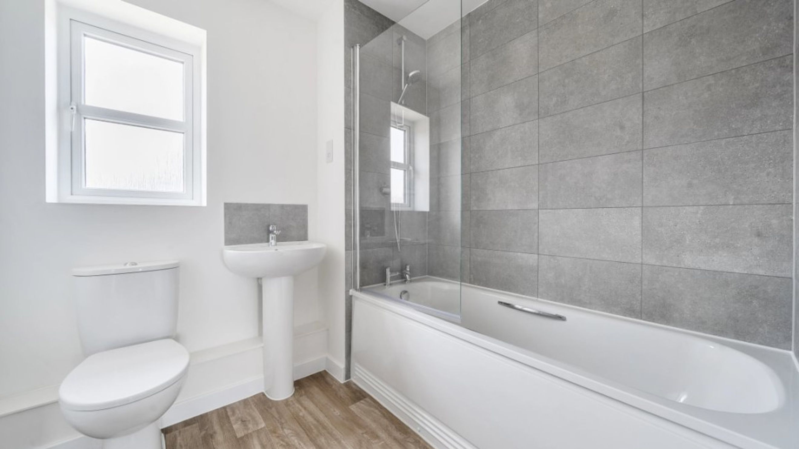 A bathroom with a bathtub, shower screen, toilet, sink, and window.