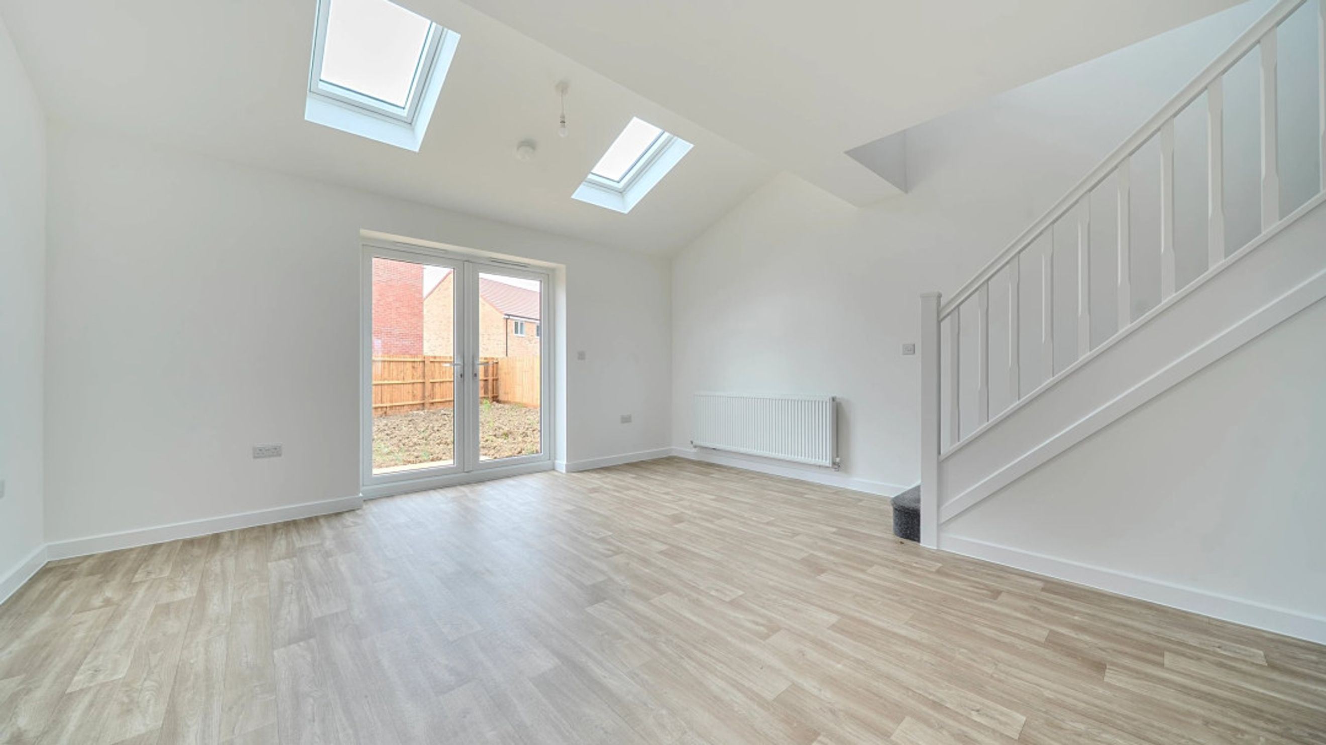 A living room with double doors, skylights, a radiator, and a staircase.