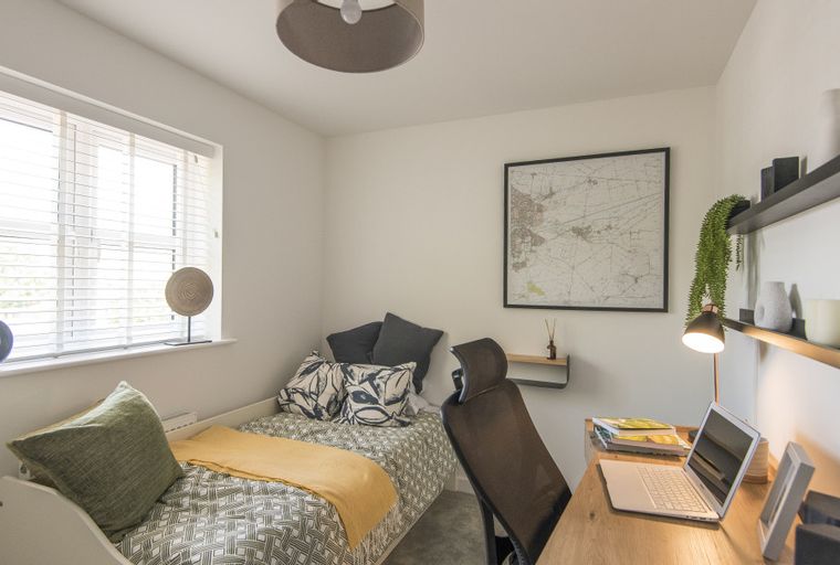 A bedroom with a single bed, a desk, and a window.