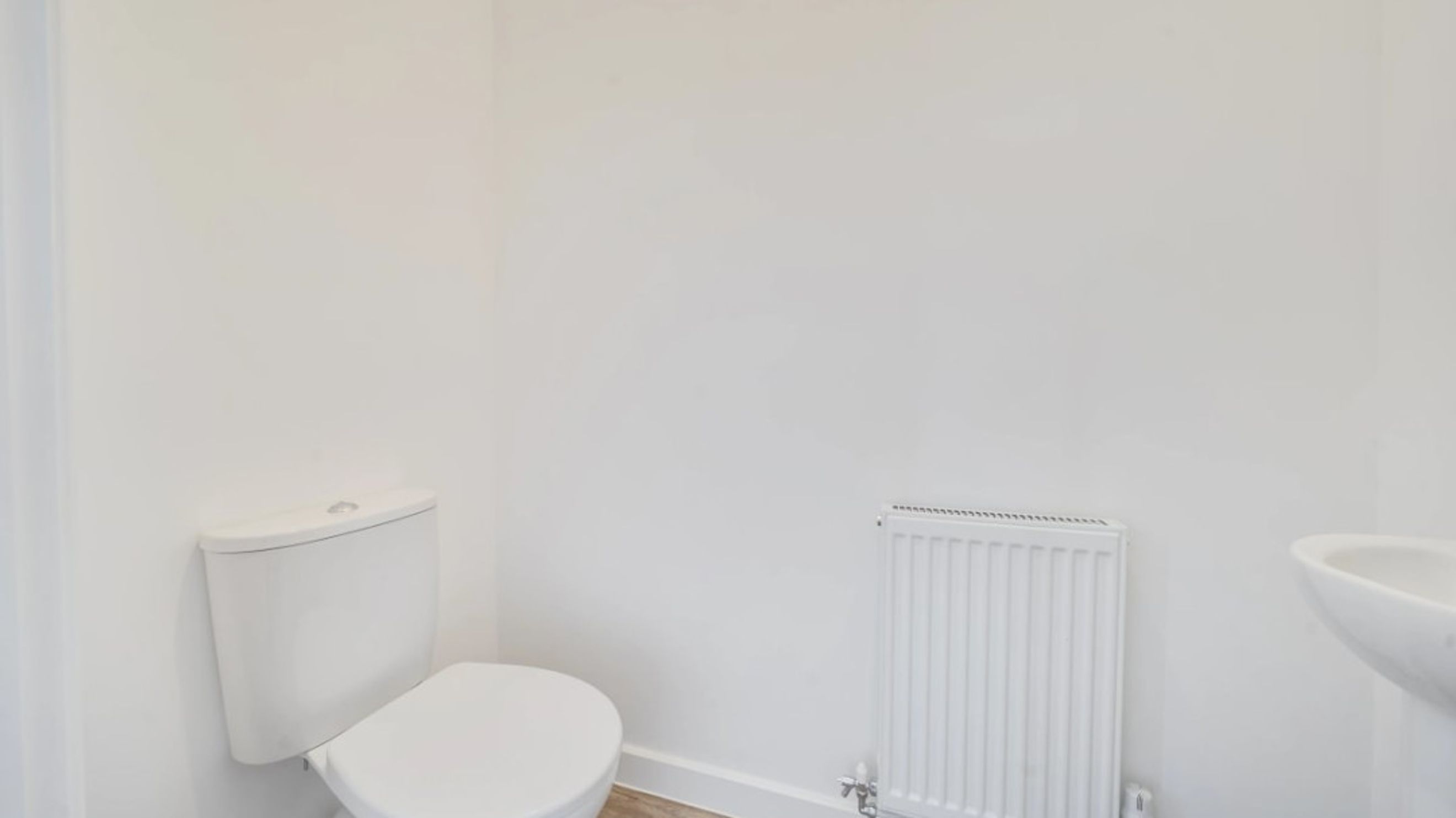 A toilet, a radiator, and a sink in a white bathroom.