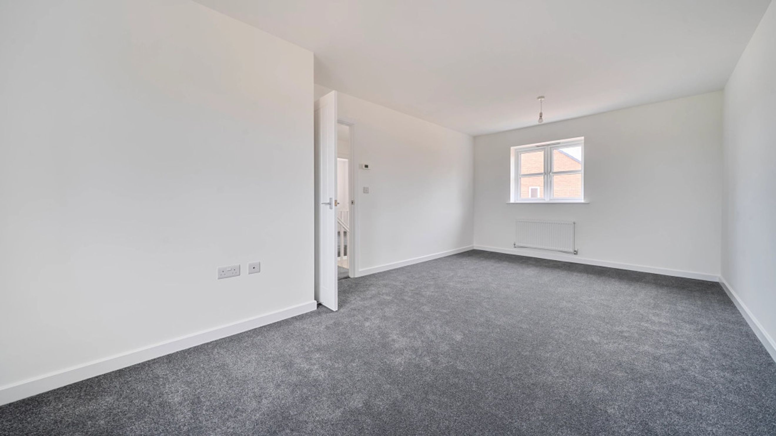 A room with a grey carpet, white walls, a window, and a doorway.