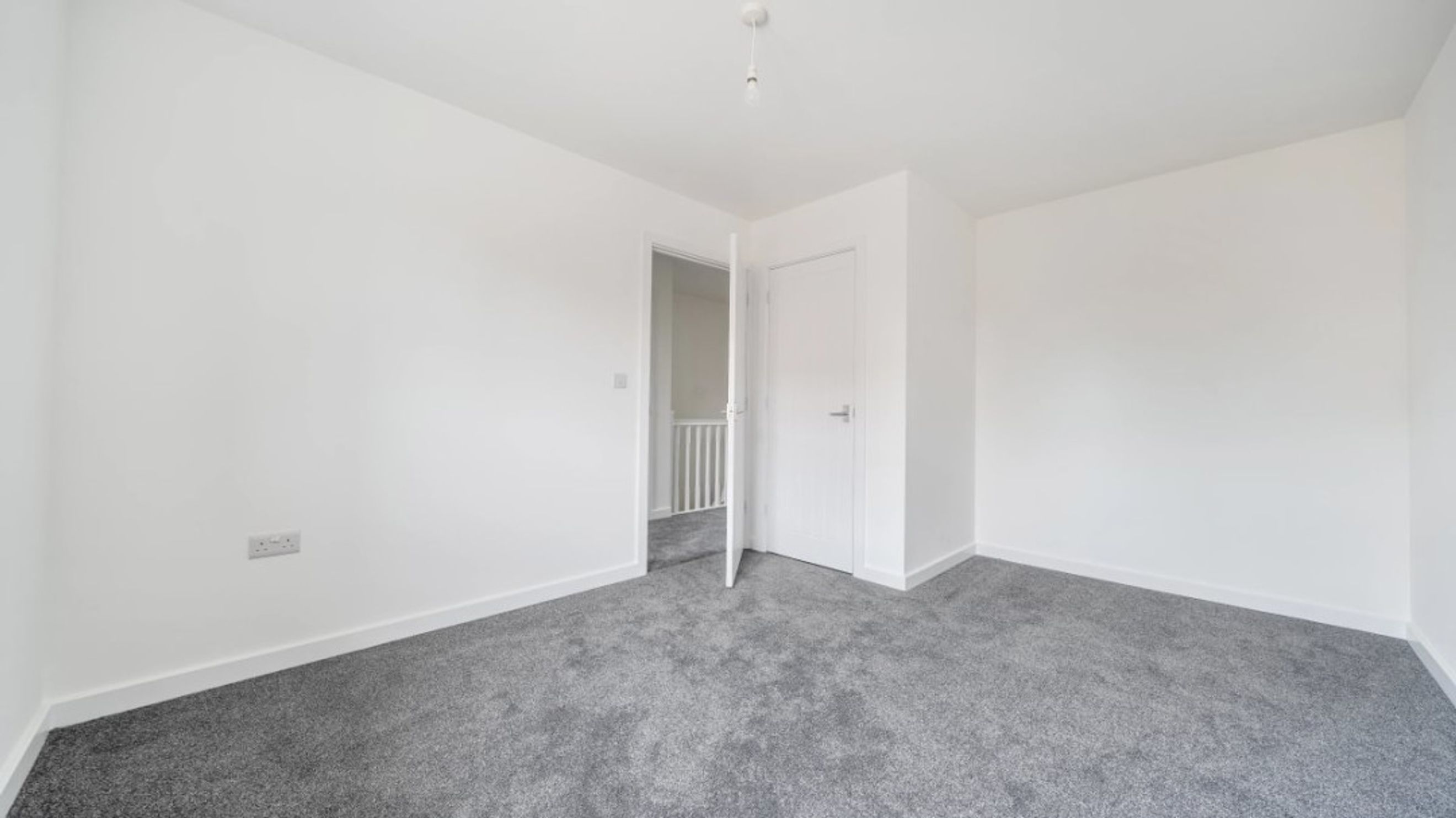 A room with white walls, grey carpet, and two doors.
