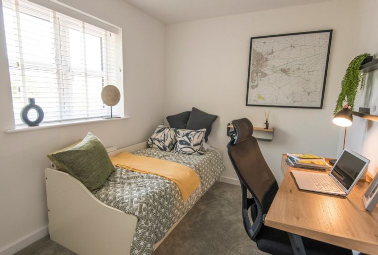 A bedroom with a single bed, a desk with a laptop, and a window.