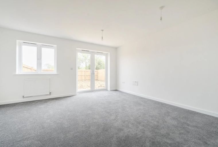 A living room with grey carpet, white walls, a window, and patio doors.