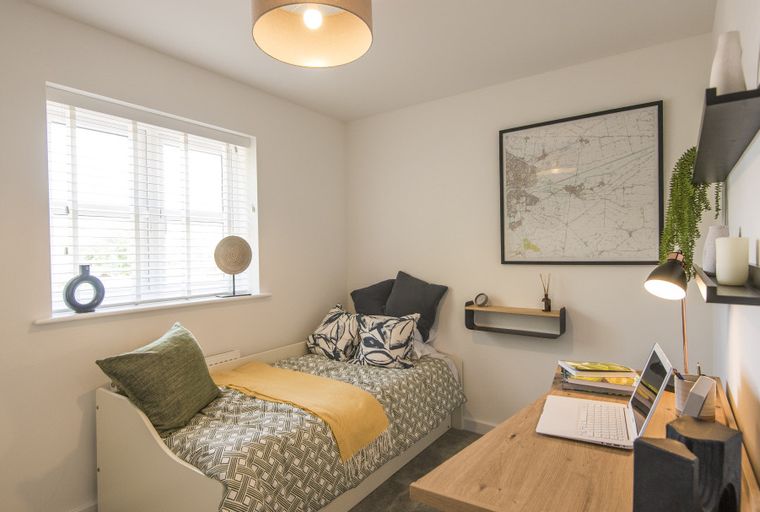 A bedroom with a single bed, a desk, and a window.