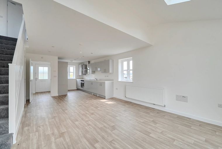 A modern open-plan living area and kitchen with a carpeted staircase and an entrance hall.