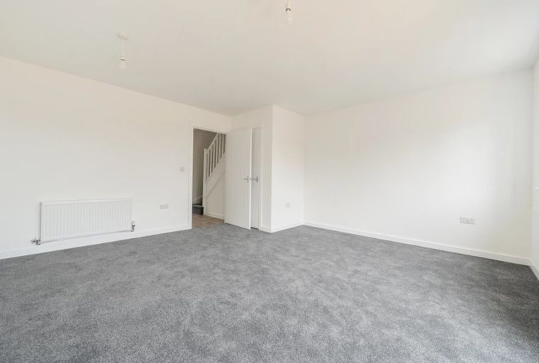 A spacious, unfurnished room with grey carpet, white walls, and a radiator.