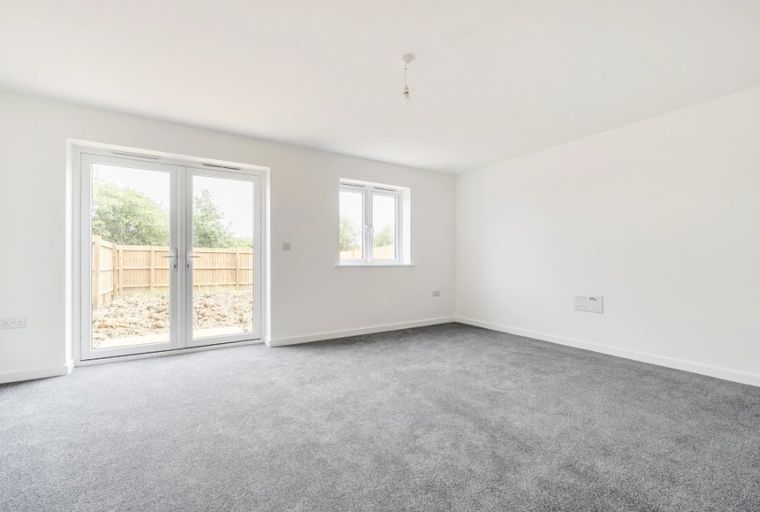 A living room with grey carpet, white walls, and double doors leading outside.