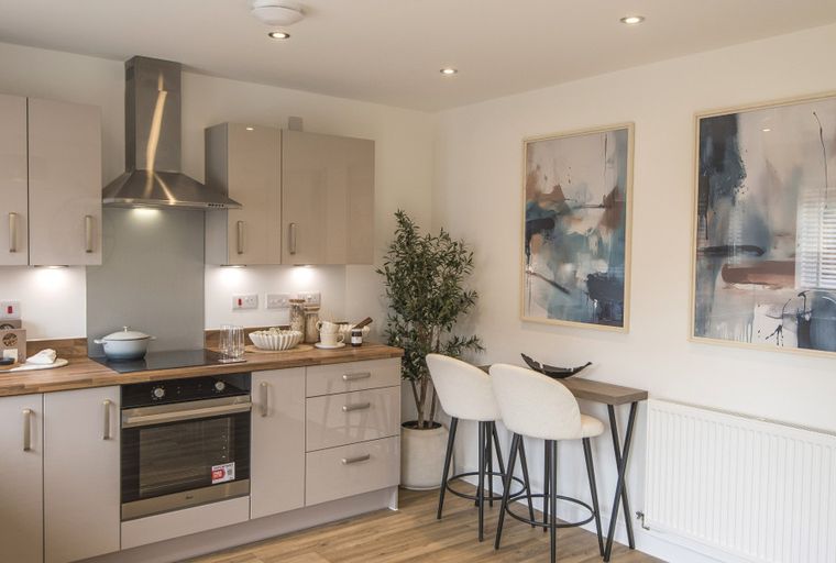 A modern kitchen with light-colored cabinets, a stainless steel range hood, an oven, and a breakfast bar with two stools.