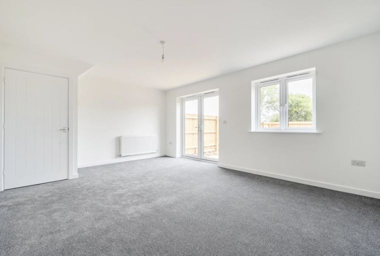 A living room with grey carpet, white walls, a radiator, double doors, and a window.
