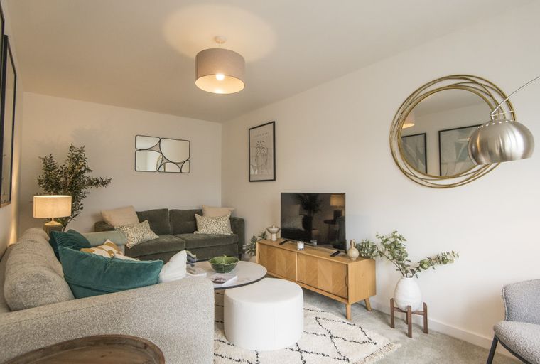 A living room with a sectional sofa, TV, media console, and a circular mirror.