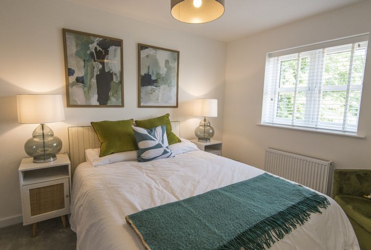 A bedroom with a bed, bedside tables, lamps, artwork, a window, and a chair.