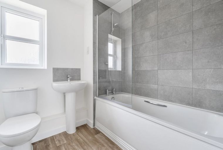 A bathroom with a bathtub, shower screen, toilet, sink, and window.