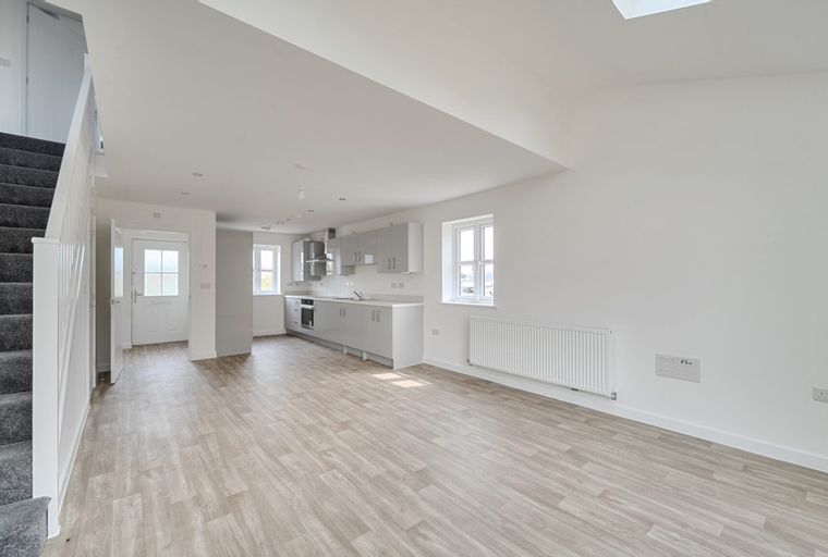 A modern open-plan living space with a kitchen, staircase, and front door.