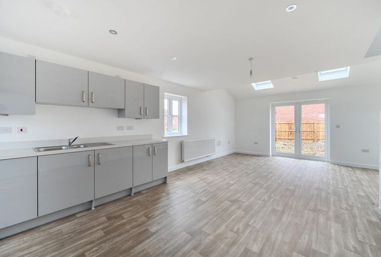 A modern open-plan kitchen and living area with grey cabinets, a double sink, and double doors leading outside.